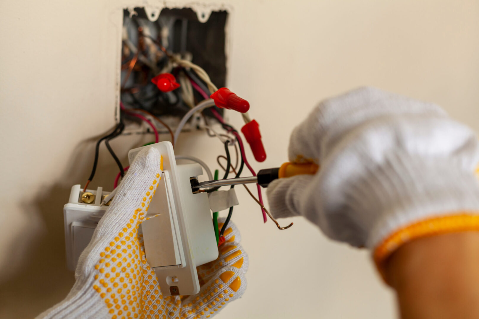 An electrician is replacing a wall switch. A DIY project concept. High voltage danger. installing wire connection using screw driver. The professional wears protective rubber gloves for safety